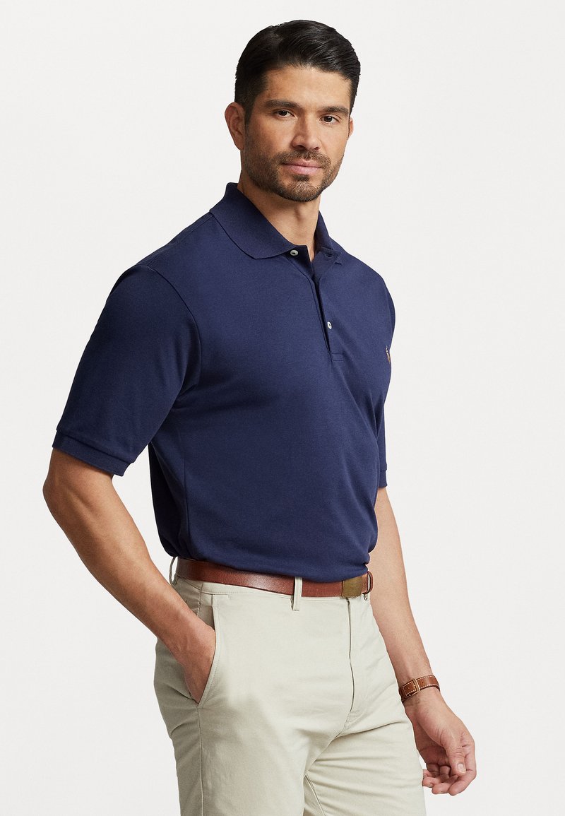 Tumši zila īsām piedurknēm polo krekls ar apkakli un divām pogām. Valkāts ar bežām biksēm un brūnu ādas jostu. Gluda auduma tekstūra.