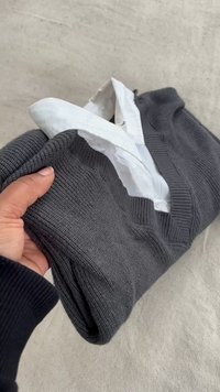 Pull en maille gris foncé avec un col en V, doté de poignets et d'un ourlet côtelés. Une chemise blanche à col est partiellement visible en dessous.