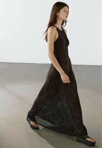Abito lungo in maglia nera con corpino aderente, design senza maniche e orlo fluttuante. Abbinato a sandali chunky con piattaforma.