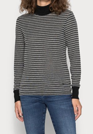 Person trägt ein graues und schwarzes langärmliges Shirt mit horizontalen Streifen, schwarzen Bündchen und Kragen, kombiniert mit blauen Jeans.