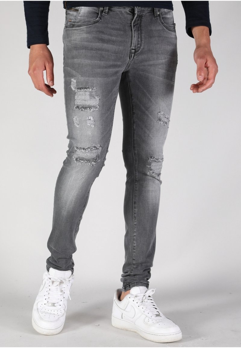 Jeans grises rasgados con un acabado deslavado, que presentan detalles desgastados en las rodillas, combinados con zapatillas blancas. Diseño de corte ajustado.
