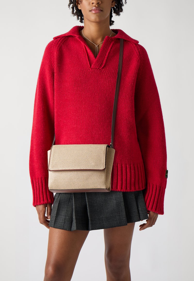 Červený pletený sveter s golierom, skombinovaný s béžovou textúrovanou crossbody taškou so zapínaním na klapku a hnedým lemovaním. Čierna plisovaná sukňa.