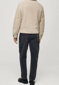 Beige Fleecejacke mit Kragen, Rückennahtdetails und dunkelgrauen schmalen Hosen. Schwarze Schuhe mit runder Spitze. Flache Textur.