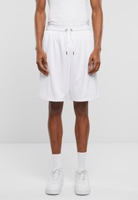 Hvite, nett basketballshorts med elastisk liv og snor. Har lommer og løs passform, kombinert med hvite sneakers og sokker.