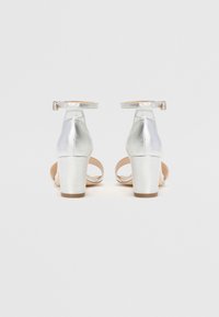 Sølvhelede sandaler med metallisk finish, ankelstropper og åpen tå-design. Kraftige hæler gir stabilitet med en jevn tekstur.