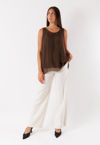 Top senza maniche marrone con una vestibilità ampia e una texture setosa. Abbinato a pantaloni bianchi a gamba larga e décolleté nere a punta.
