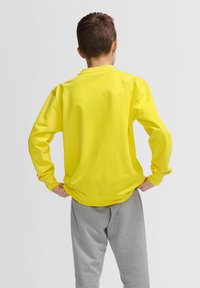 Långärmad gul sweatshirt i bomull, med rund halsringning och ribbad mudd, i kombination med gråa joggingsbyxor.