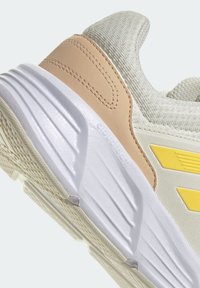 Scarpa da corsa leggera con tomaia in tessuto grigio traspirante, dettagli in pelle beige e suola intermedia bianca con scanalature textures.