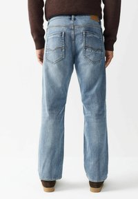 Gai zili džinsi ar brīvu piegriezumu, ar aizmugures kabatām un norādītām flapiem, kā arī brūnu ādas plāksteri uz jostas vietas.