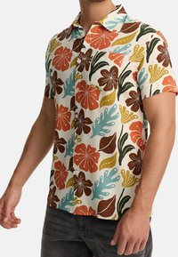 Camisa de botones de manga corta con un patrón floral en rojo, naranja, verde y azul sobre un fondo claro. Incluye un bolsillo en el pecho.