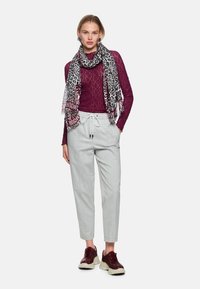 Weinrotes Langarmoberteil, hellgraue, zulaufende Hose und ein schwarz-weißes Leopardenmuster-Schal. Braune Sneakers mit beigen Sohlen.