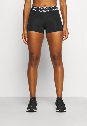 Athlet trägt schwarze Nike Pro Kompressionsshorts und schwarze Nike Laufschuhe, steht vor einem einfachen weißen Hintergrund.