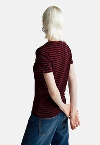 Pruhované vínové tričko vyrobené z měkké tkaniny, s krátkými rukávy a přiléhavým střihem. Nosené s modrými džíny, vyzařující ležérní styl.