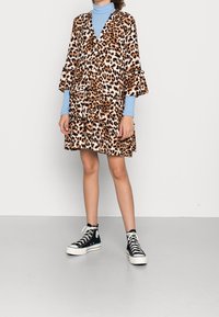 Abito a strati con stampa leopardata e maniche a campana, abbinato a un dolcevita blu chiaro e sneakers alte nere. Tessuto strutturato.