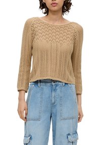 Beige gestrickter Pullover mit einem strukturierten Muster, weitem Ausschnitt und Dreiviertelärmeln, kombiniert mit lockeren, hellblauen Denim-Cargohosen.