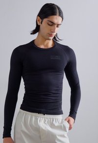 Camisola preta de mangas compridas, ajustada, com padrões texturizados e decote redondo, combinada com calções de cor clara.