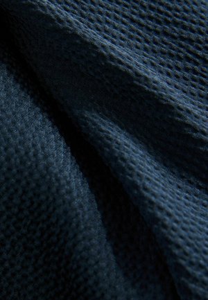Tessuto blu scuro con una trama a nido d'ape. Il materiale appare morbido e leggermente riflettente, mostrando pieghe e una leggera lucentezza.