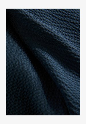 Texturiertes dunkelblaues Gewebe mit einem Waffelmuster. Das Material wirkt weich und leicht reflektierend, mit sichtbaren Falten und einem subtilen Glanz.