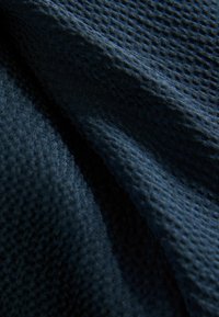 Tessuto blu scuro con motivo strutturato simile a un alveare e pieghe morbide che creano ombre e riflessi sulla superficie.