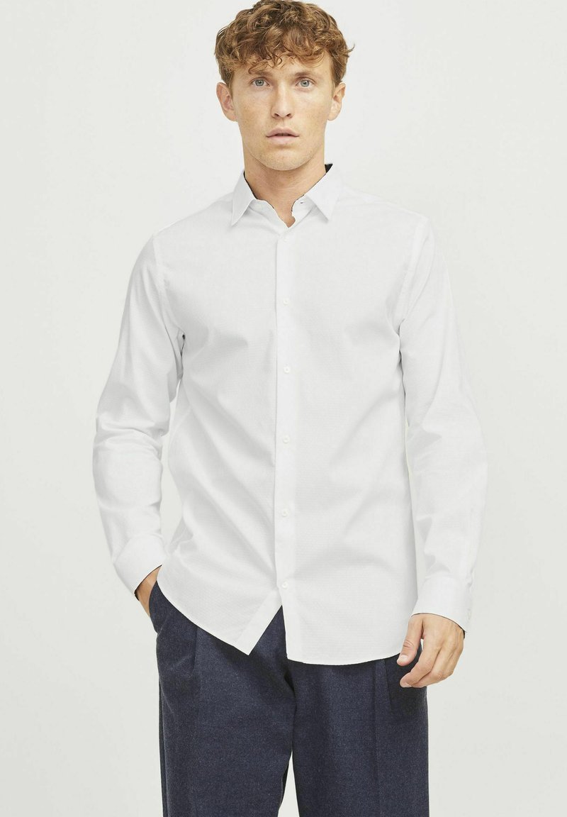 Camisa blanca de manga larga tipo polo con un cuello estándar, fabricada con un tejido estructurado y un acabado ligeramente texturizado.