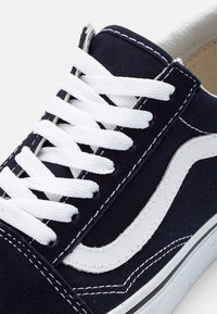 Marineblaues Segeltuch-Sneaker mit weißen Schnürsenkeln, weißem Seitenstreifen und kontrastierenden Nähten, hervorgehoben durch eine Gummisohle und strukturierten Stoff.