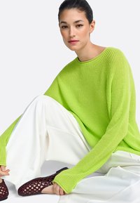 Jasnozielony, dziany sweter z długimi rękawami, zestawiony z luźnymi białymi spodniami i bordowymi butami na sznurowadła. Teksturowana tkanina, casualowy design.