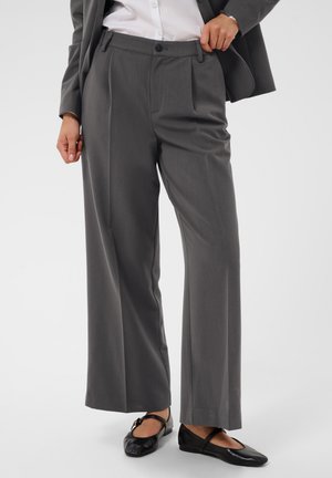 Personne portant un pantalon gris à jambes larges, une chemise blanche, un blazer gris et des ballerines Mary Jane noires avec une bride à boucle.
