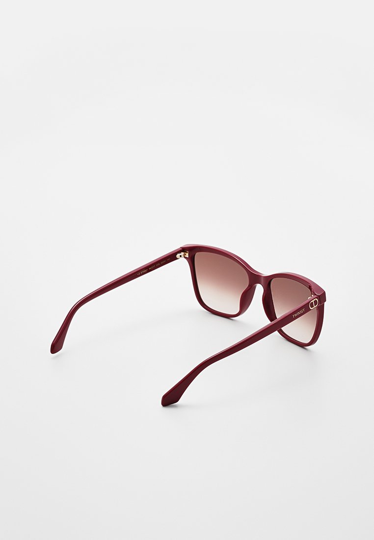 Occhiali da sole bordeaux con lenti sfumate, forma rettangolare e bracci larghi con un logo in oro sul lato.