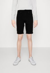 Svarte denimshorts med rullekanter, med et klassisk femlommersdesign. Bæres med en lys grå langermet skjorte og grå joggesko.