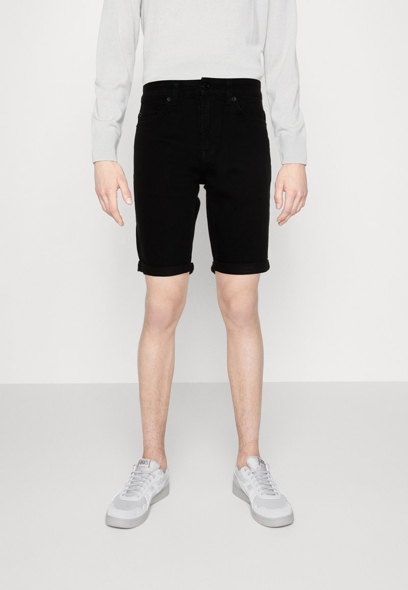 Svarte denimshorts med rullekanter, med et klassisk femlommersdesign. Bæres med en lys grå langermet skjorte og grå joggesko.