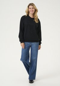Zwarte sweatshirt met een gestructureerd bladontwerp, gecombineerd met wijde blauwe jeans. De stof ziet er zacht uit met een comfortabele pasvorm.