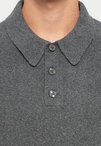 Polo de punto gris con cuello, tapa de tres botones y tejido texturizado. Detalles sutiles de canalé en el cuello y la tapa.