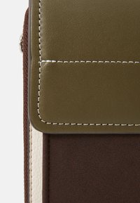 Accessorio compatto realizzato in pelle verde e tessuto texturizzato marrone, con cuciture bianche e un design a patta strutturata.