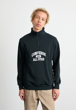 Sudadera de forro polar verde oscuro con media cremallera, con dobladillo y puños acanalados. Presenta el texto blanco "CONVERSE 1908 ALL STAR" centrado en la parte frontal.