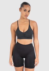 Mustat urheilurintaliivit, joissa on ohuet hihnat ja kerätty yksityiskohta edessä, yhdistettyinä korkeavyötäröisiin mustiin pyöräilyshortseihin, jotka ovat sileää ja joustavaa kangasta.