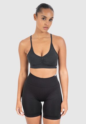Sujetador deportivo negro con tirantes finos y detalle fruncido en la parte delantera, combinado con shorts de bicicleta negros de tiro alto en una tela suave y elástica.