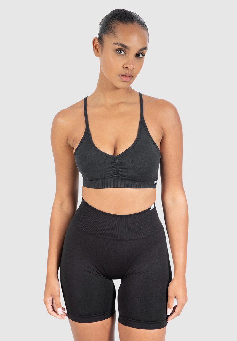 Mustat urheilurintaliivit, joissa on ohuet hihnat ja kerätty yksityiskohta edessä, yhdistettyinä korkeavyötäröisiin mustiin pyöräilyshortseihin, jotka ovat sileää ja joustavaa kangasta.