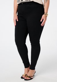 Zwarte stretchjeans met een slim fit, voorzien van riemlussen en voorzakken. Gecombineerd met open teen zwarte hakken met gouden accenten.