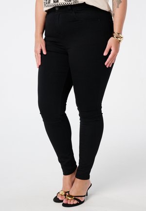 Jean stretch noir à coupe ajustée, avec passants de ceinture et poches avant. Associés à des sandales à talons ouverts noires avec des accents dorés.