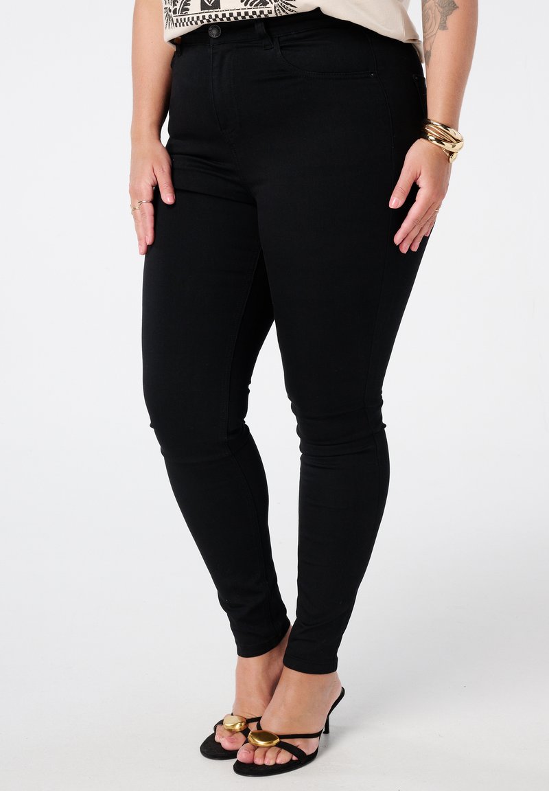 Zwarte stretchjeans met een slim fit, voorzien van riemlussen en voorzakken. Gecombineerd met open teen zwarte hakken met gouden accenten.