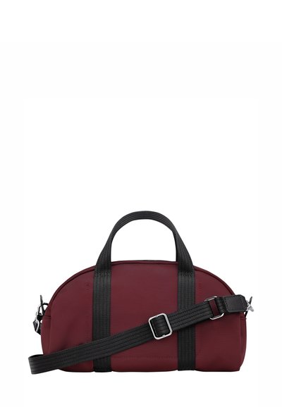 Kleine scharlachrote Reisetasche mit schwarzen Griffen und einem verstellbaren schwarzen Schultergurt vor einem weißen Hintergrund.