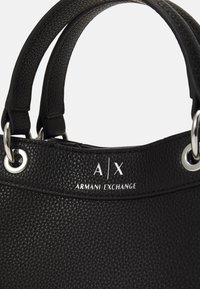 Fekete textúrált bőr kézitáska, dupla fogantyúval, ezüstszínű fémrészletekkel és "A/X" valamint "ARMANI EXCHANGE" felirattal ellátott dombornyomott logóval.