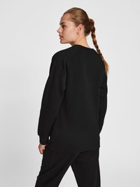 Zwarte sweatshirt met een relaxte pasvorm, lange mouwen en ronde hals. Zachte textuur, ribgebreide manchetten en zoom, gedragen met bijpassende zwarte broek.