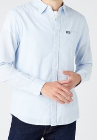 Camicia a maniche lunghe azzurro chiaro realizzata in tessuto a righe, con collo button-down, taschino sul petto e logo del marchio discreto sulla tasca.