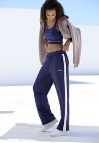 Tumed särgid sinised dressipüksid valgete külgtükkide ja nupudega; koos vastava tumeda lühikese toppiga ja beeziga ülepaisutatud kapuutsiga.