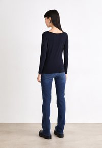 Navy long-sleeve fitted top with a wide neckline, paired with classic blue jeans. Flared legs and black platform boots complete the outfit.