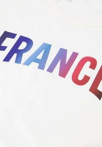 T-shirt blanc avec un grand texte "FRANCE" dégradé du bleu au rouge, doté d'un col rond et d'une texture de tissu douce.