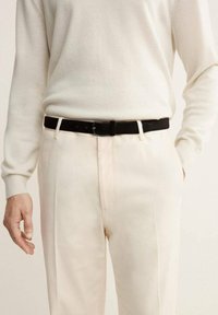 Suéter de lana de color claro combinado con pantalones color crema, sujetado con un cinturón negro. La tela parece suave, con una textura lisa y un brillo sutil.