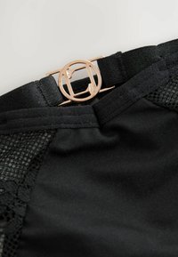 Zwart kledingstuk met gaas en kantdetails. Bevat een gouden metalen sluiting bij de taille. Materiaal is glad met een lichte glans.