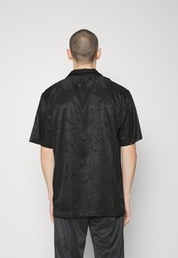 Lyhythihainen musta paita, jossa on hienovarainen, teksturoitu kukkakuosi; sileä kangas; klassinen kaulus; rento malli; irrallisena.